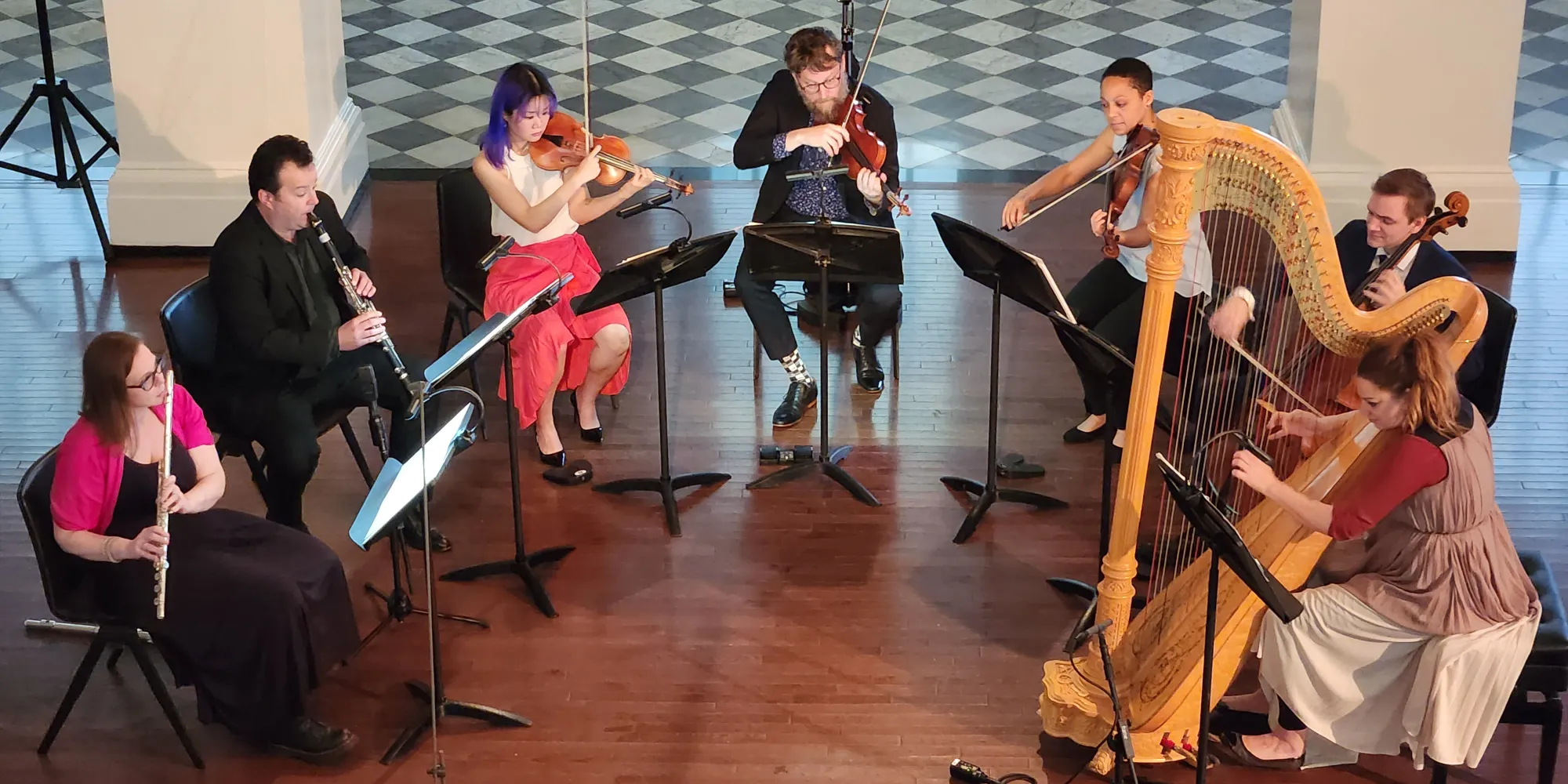 A collection of musicians sit in a semi-circle to perform in St. Paul's Chapel